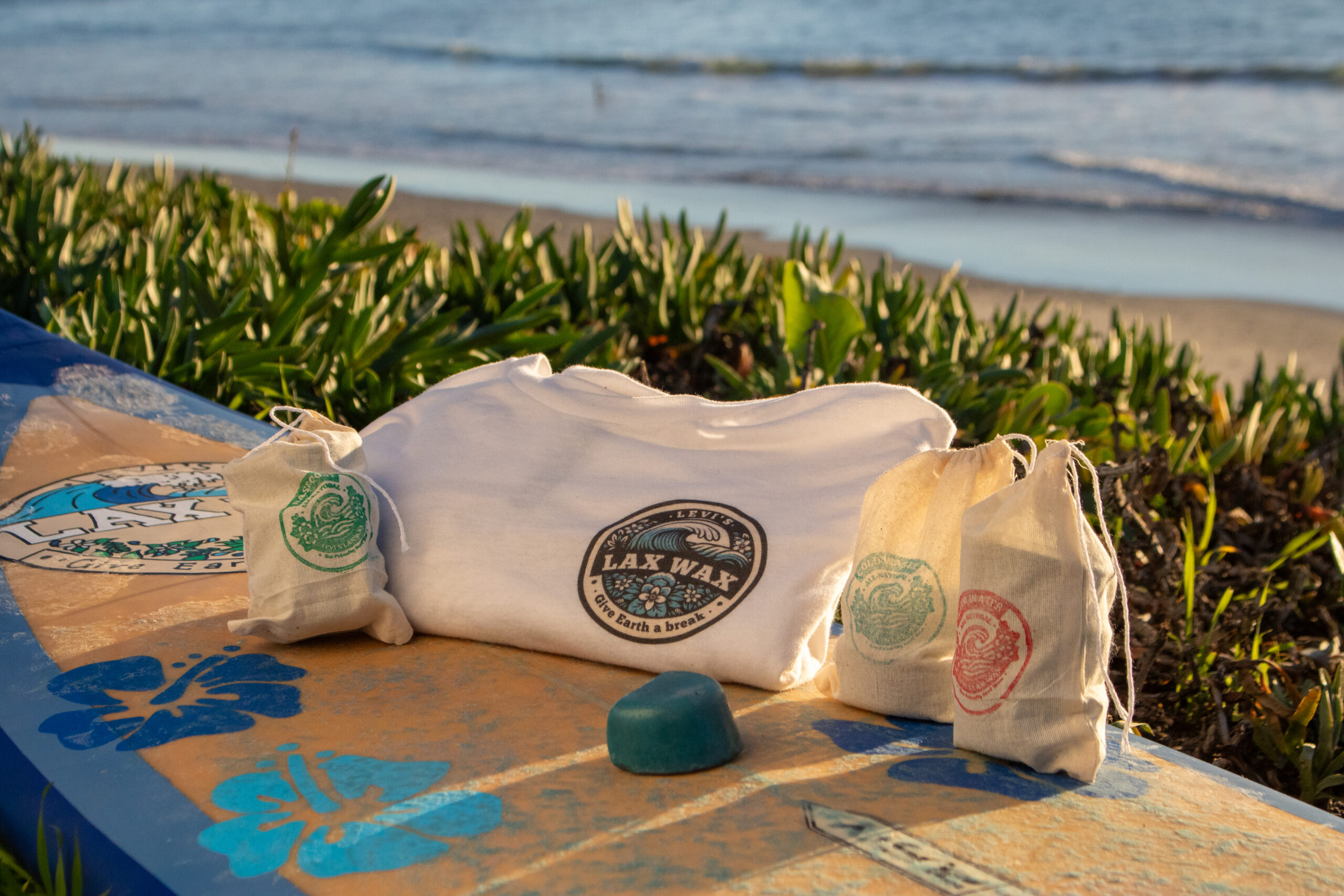 Assorted collection of Lax Wax's product offerings at the beach on a surfboard